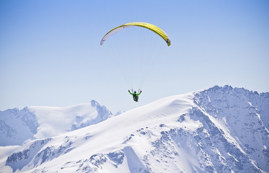Paraglider with yellow wing above snowy mountains