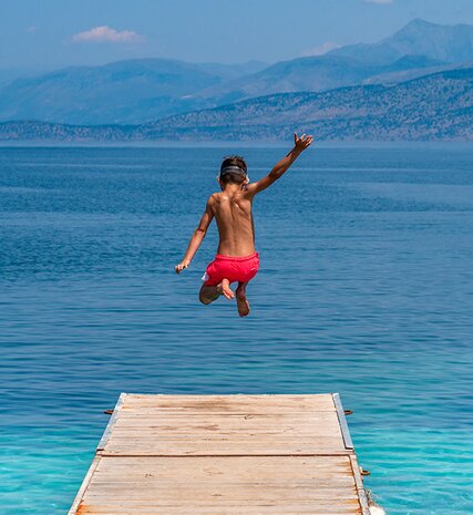 Boy jumping off wooden jetty into bright blue sea