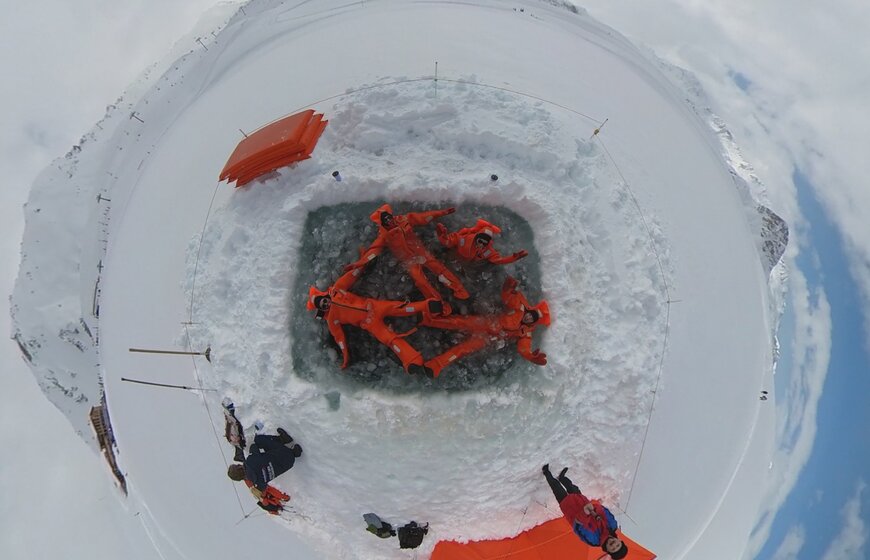 Aerial view of four people in orange drysuits floating on ice 