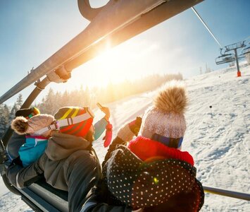 Four people on chairlift with sun in background