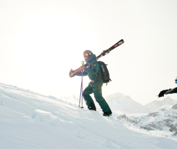 Two skiers hiking up slope with skis on shoulders