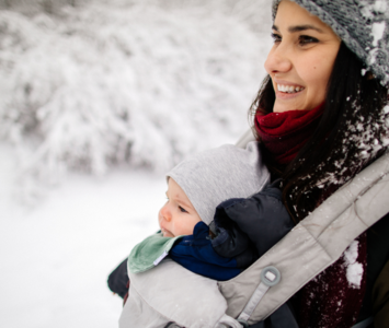 Woman wearing young baby in baby carrier in snow