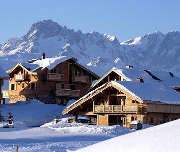 sunny photo of snow covered chalets in Alpe d'huez with mountains in the background
