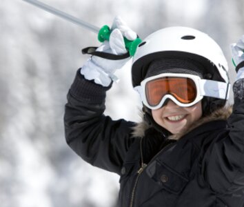 Child in ski helmet and goggles waving ski poles in the air