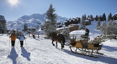 Horse-drawn sleigh and walkers in Avoriaz on sunny day