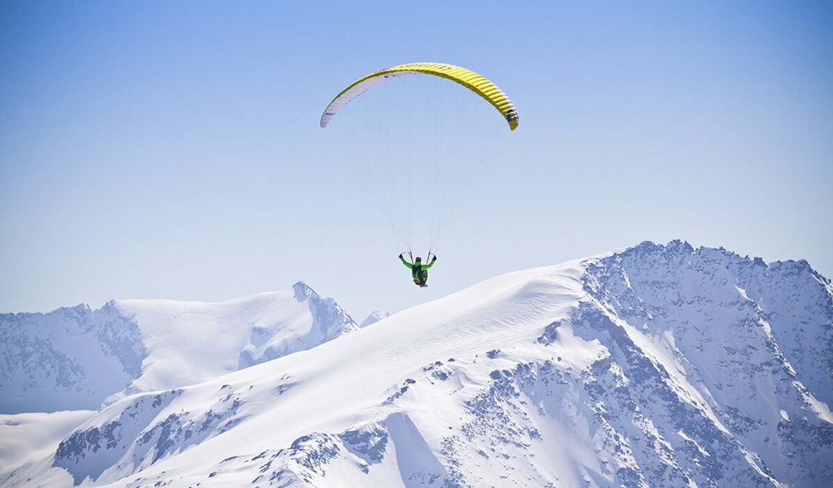 Person paragliding over snowy mountain