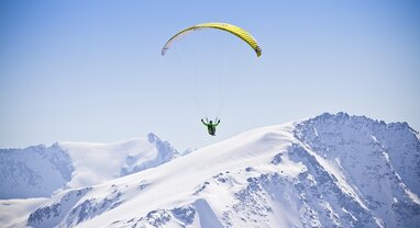 Person paragliding over snowy mountain