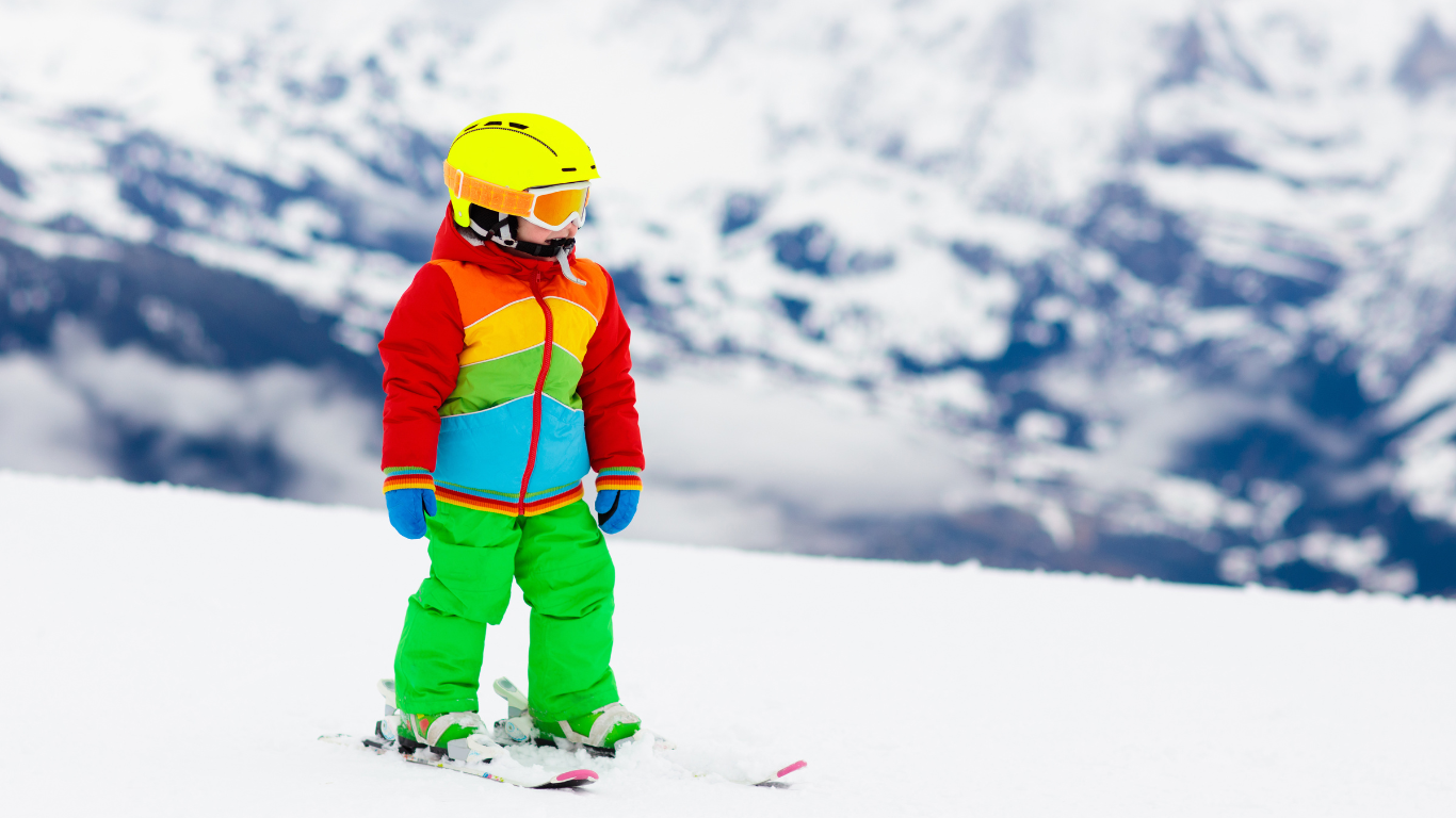 Young child in bright-coloured ski wear skiing on gentle slope