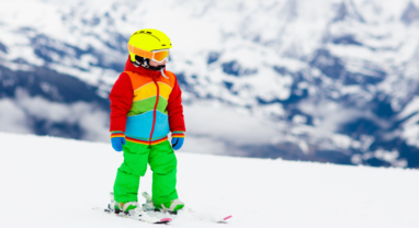 Young child in bright-coloured ski wear skiing on gentle slope
