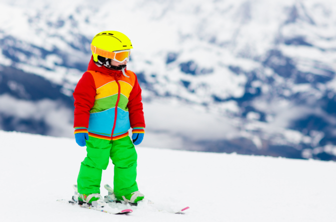 Young child in bright-coloured ski wear skiing on gentle slope