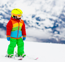Young child in bright-coloured ski wear skiing on gentle slope
