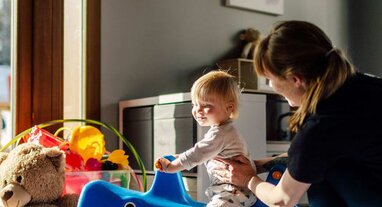 Smiling baby on rocking toy with nanny in Bear Cubs playroom