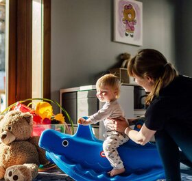 Smiling baby on rocking toy with nanny in Bear Cubs playroom