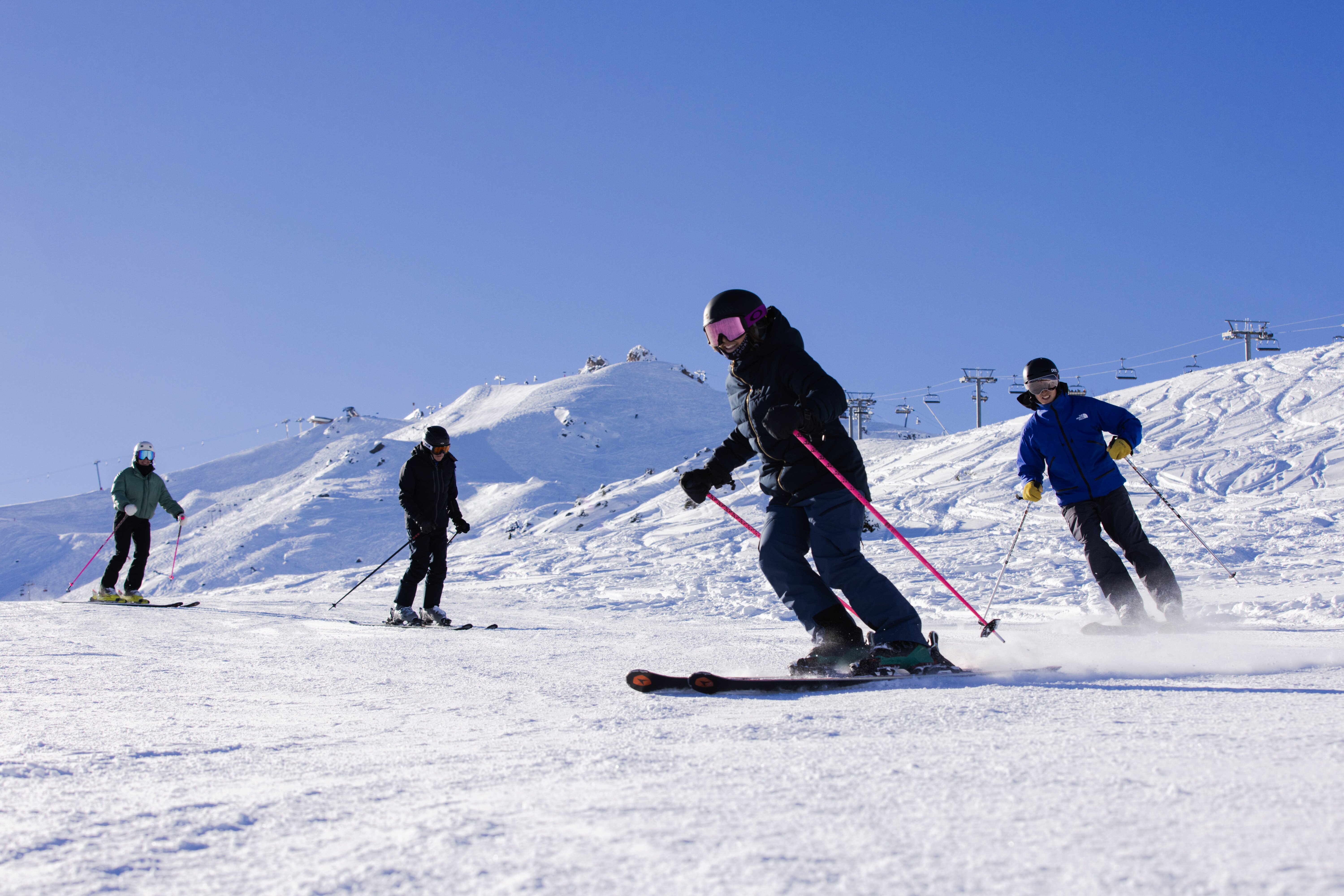 3 skiers following ski instructor down slope