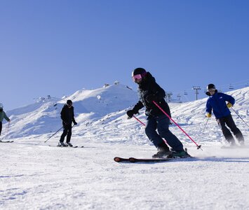 3 skiers following ski instructor down slope