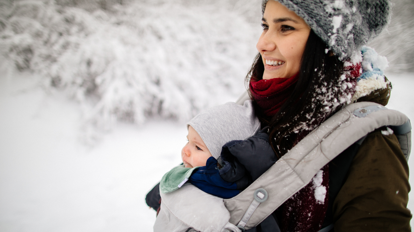 Woman wearing young baby in baby carrier in snow