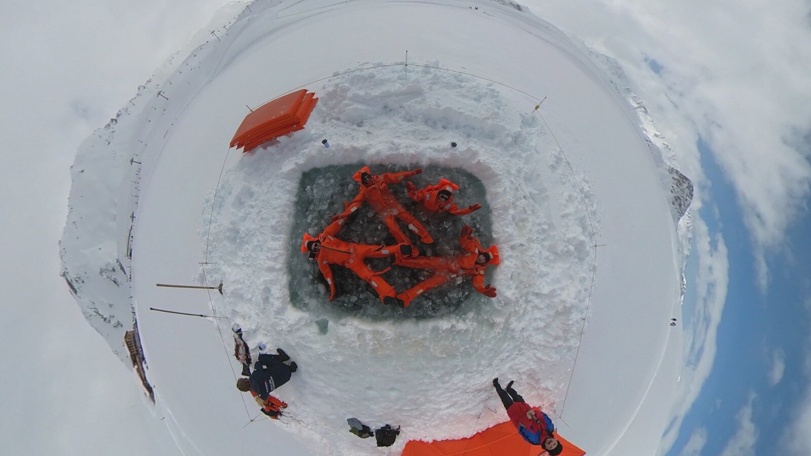 Aerial view of four people in orange drysuits floating on ice