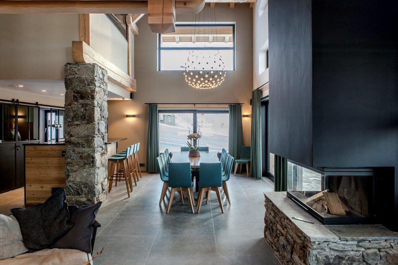 Contemporary living area with long dining table, bar area and log fire in luxury ski chalet CLUB 21Forty in Les Arcs by VIP SKI
