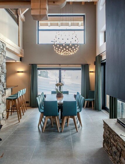 Contemporary living area with long dining table, bar area and log fire in luxury ski chalet CLUB 21Forty in Les Arcs by VIP SKI