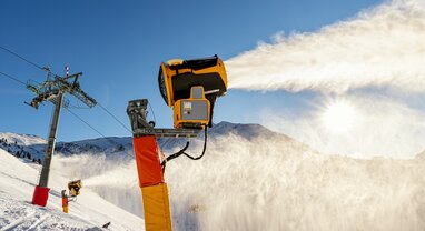 Snow cannons producing snow on ski runs on sunny day