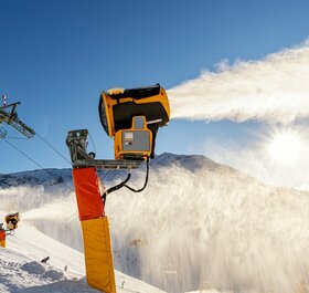 Snow cannons producing snow on ski runs on sunny day