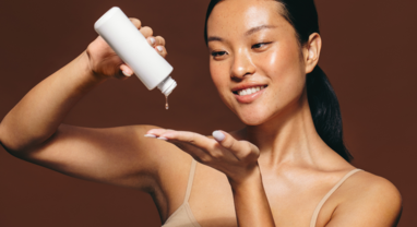Smiling woman pouring skincare product out of bottle onto hand