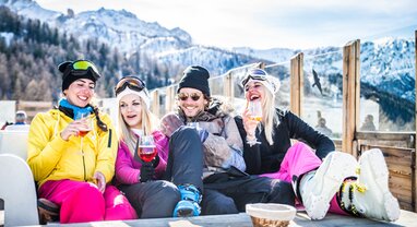 Four friends in ski clothing sitting on mountain restaurant terrace with drinks