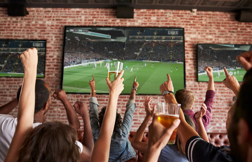 Back view of people watching football together on big screens in a bar