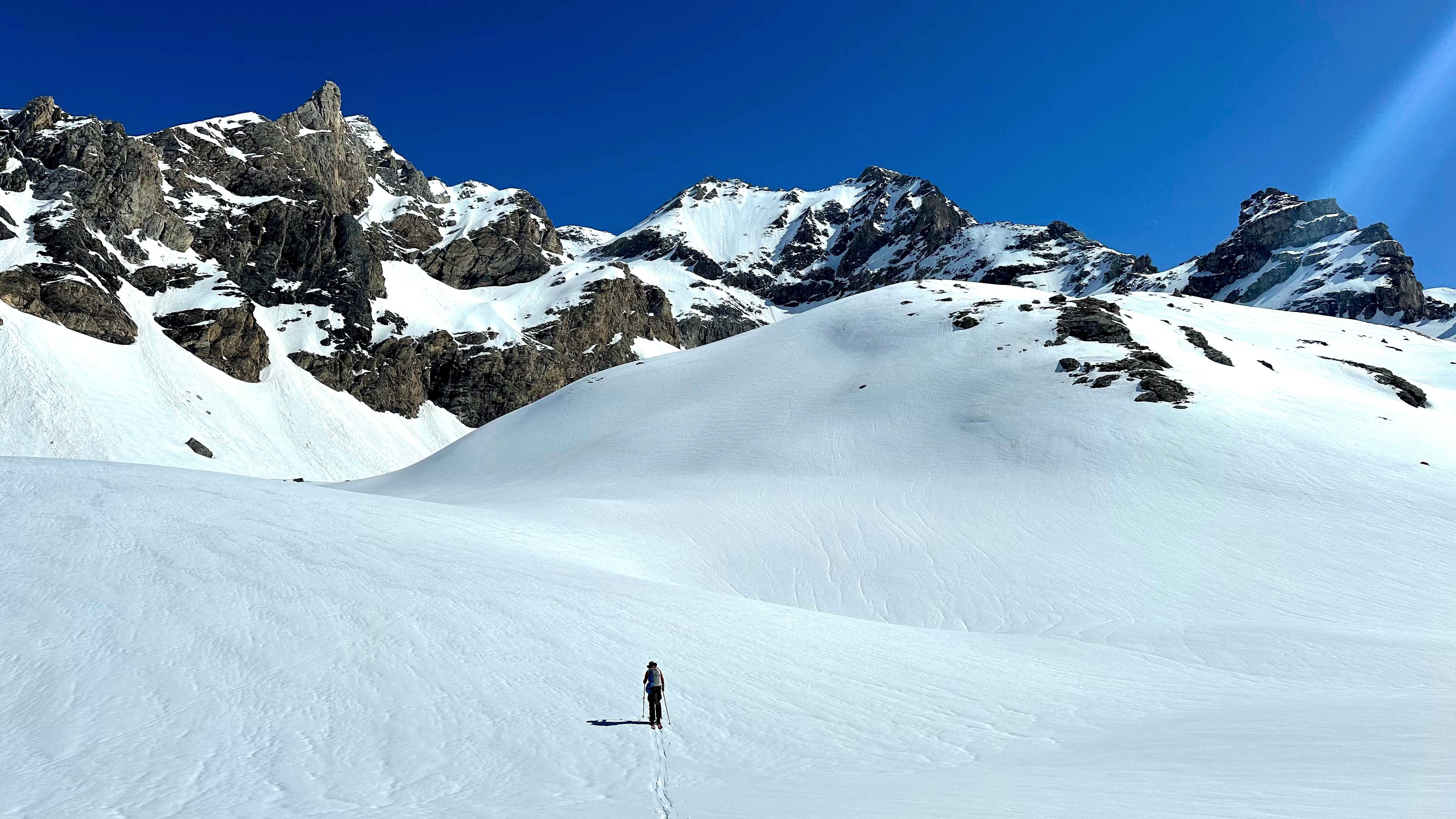 Person ski touring from a distance on a blue sky day