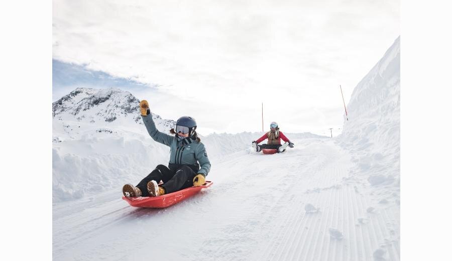 Two women sleding down hill with arms in the air