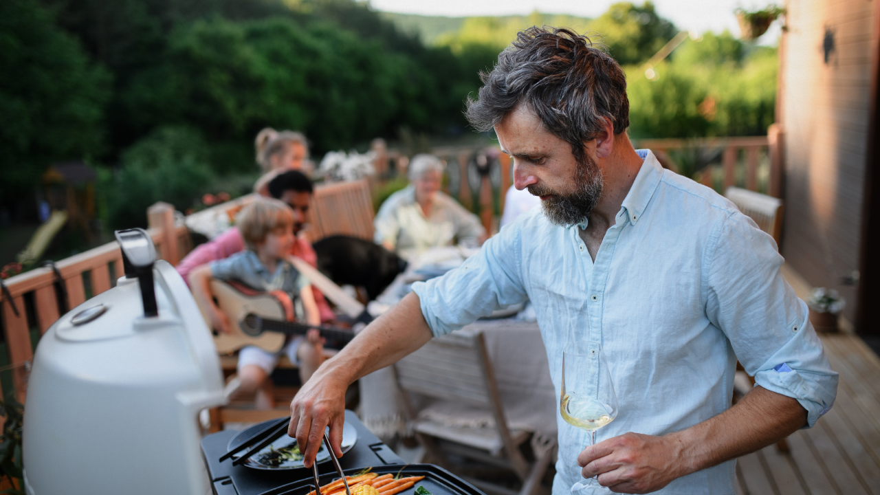 Man holding glass of wine cooking food on BBQ