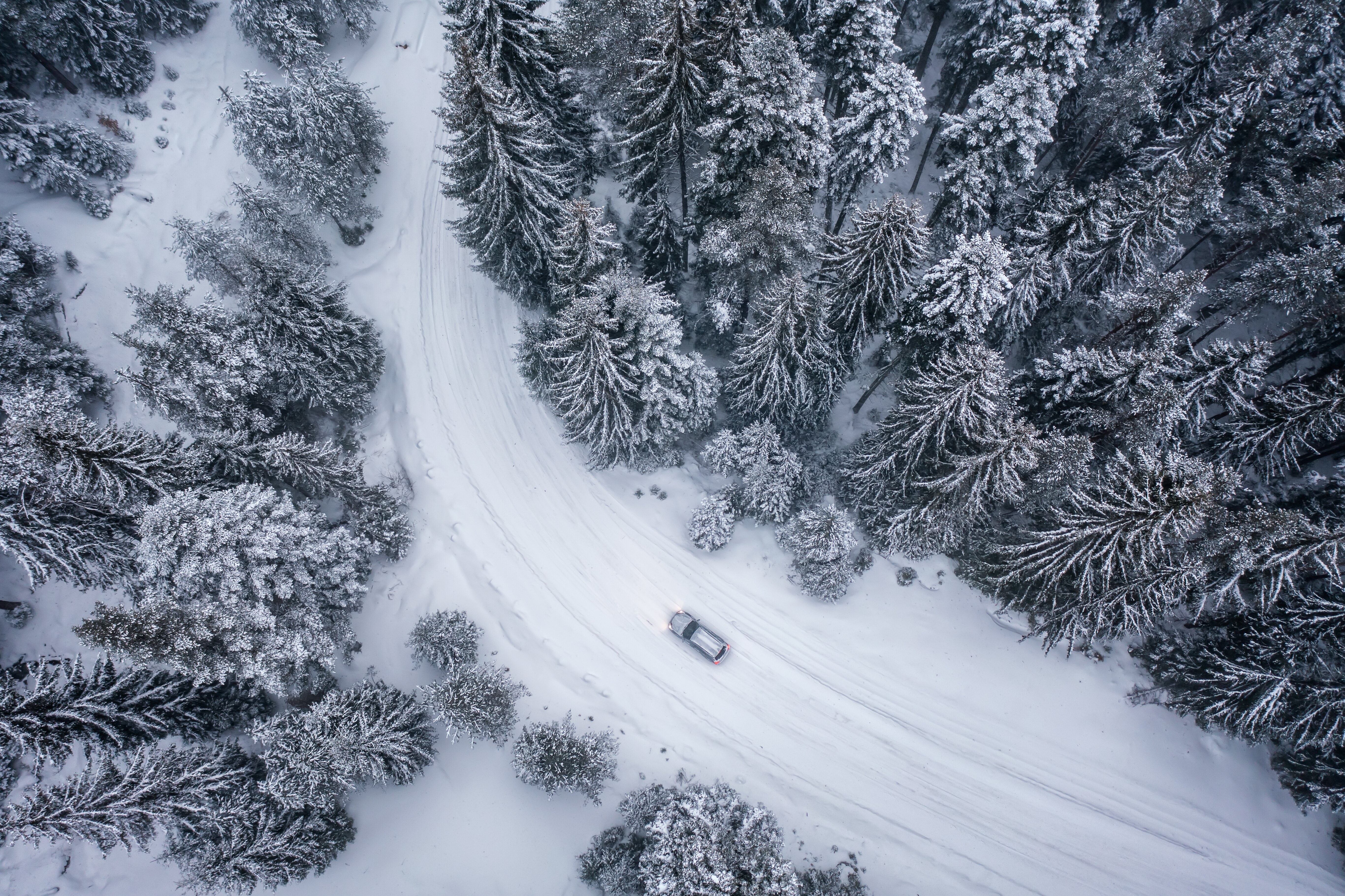 Aerial view of silver car driving along snowy road