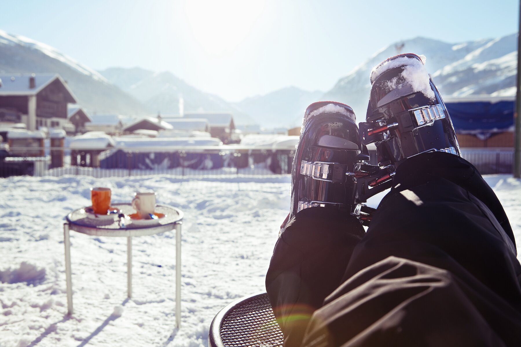 Skier resting ski boots on coffee table on terrace by ski slopes