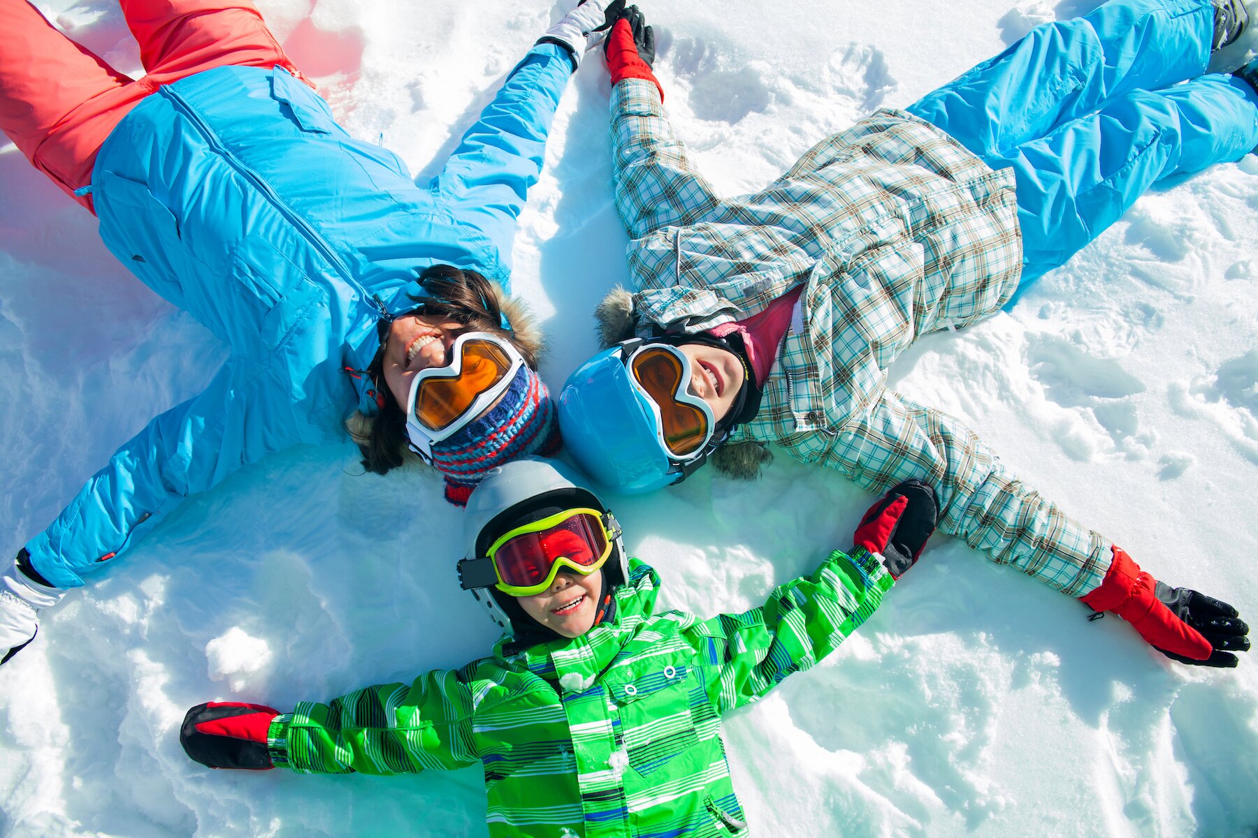 family laying in the snow with ski goggles
