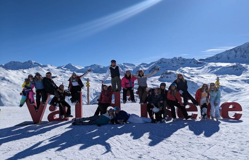 Smiling VIP SKI seasonnaires sitting on Val d'Isere letters