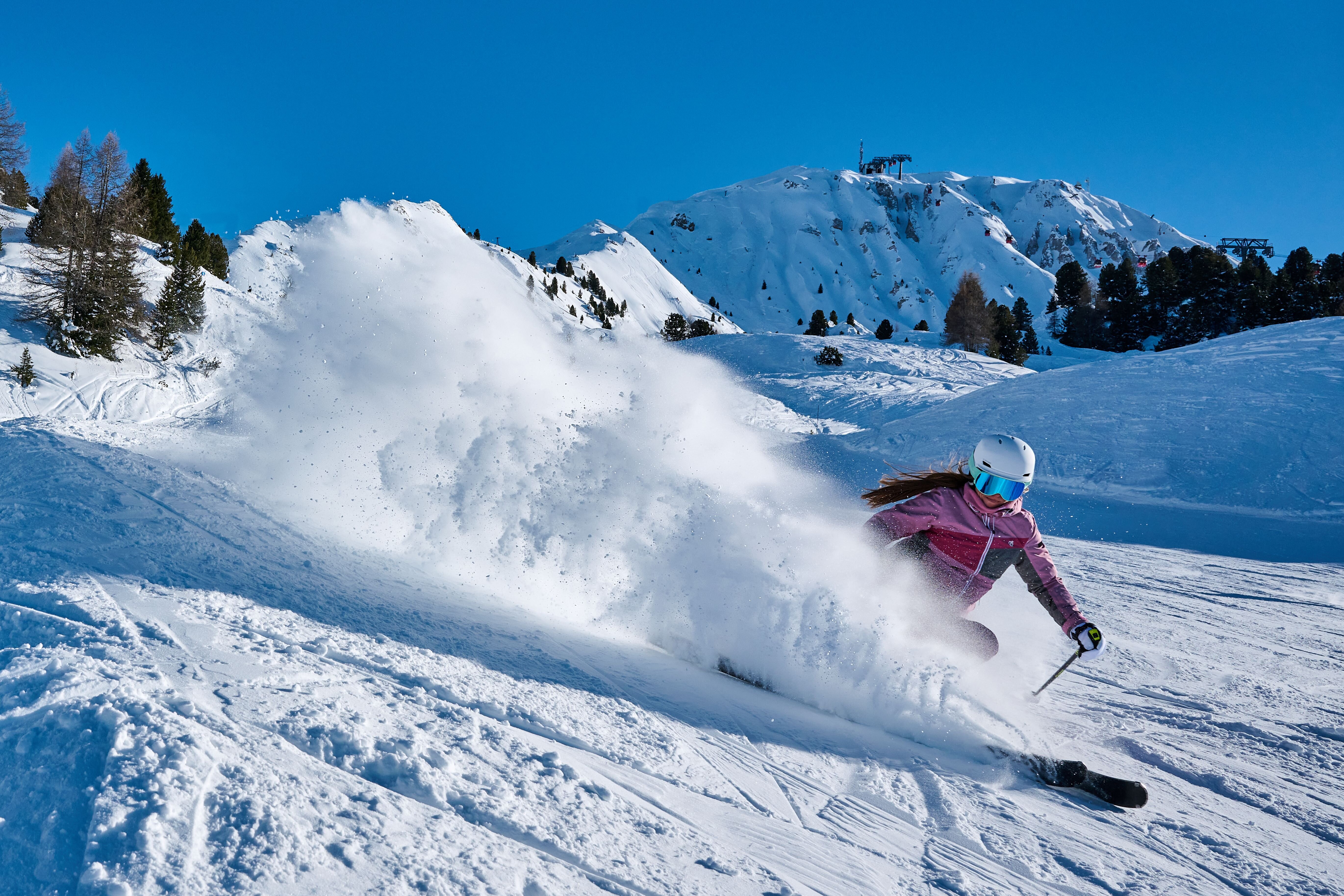 Female skier in pink ski suit skiing and spraying snow in La Plagne