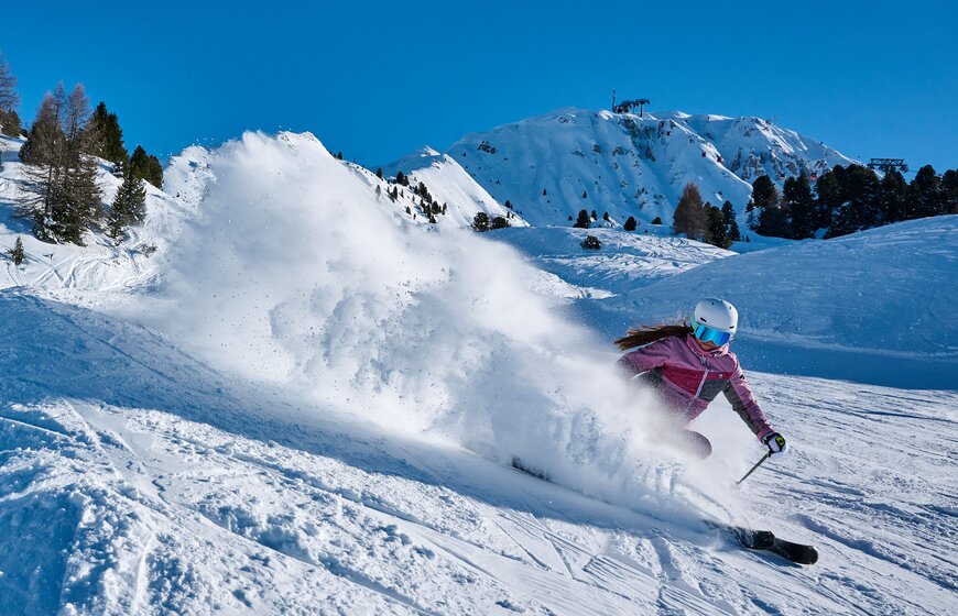Smiling female skier in pink ski jacket and white helmet spraying snow with skis in La Plagne