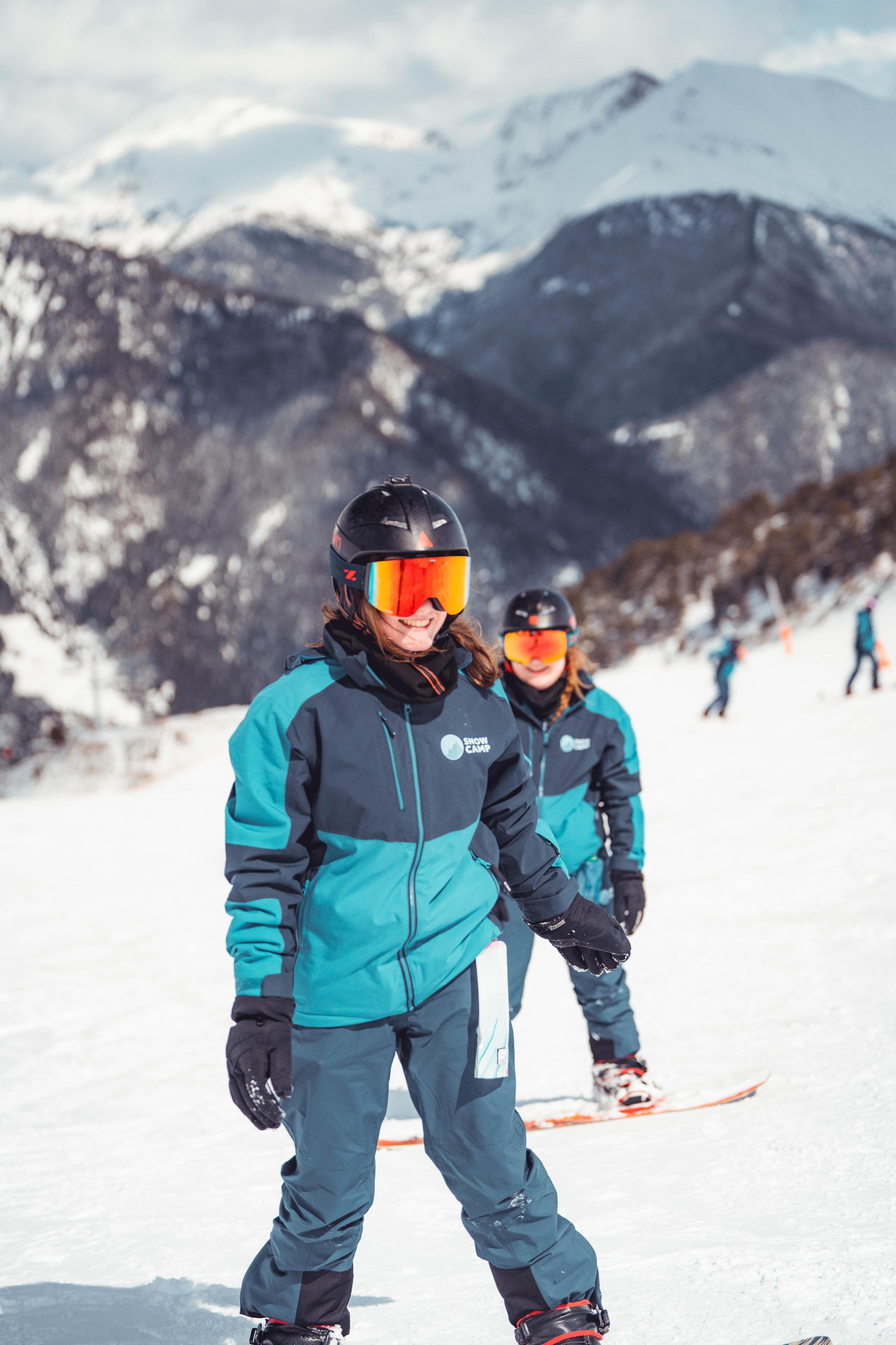 Two smiling young women on snowboards on the piste