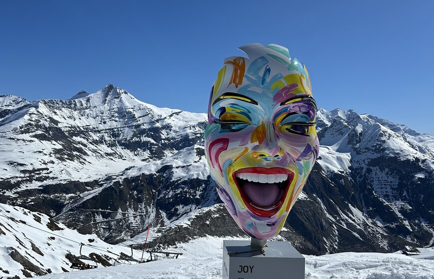 Smiling painted face sculpture in Tignes with blue sky and snowy background