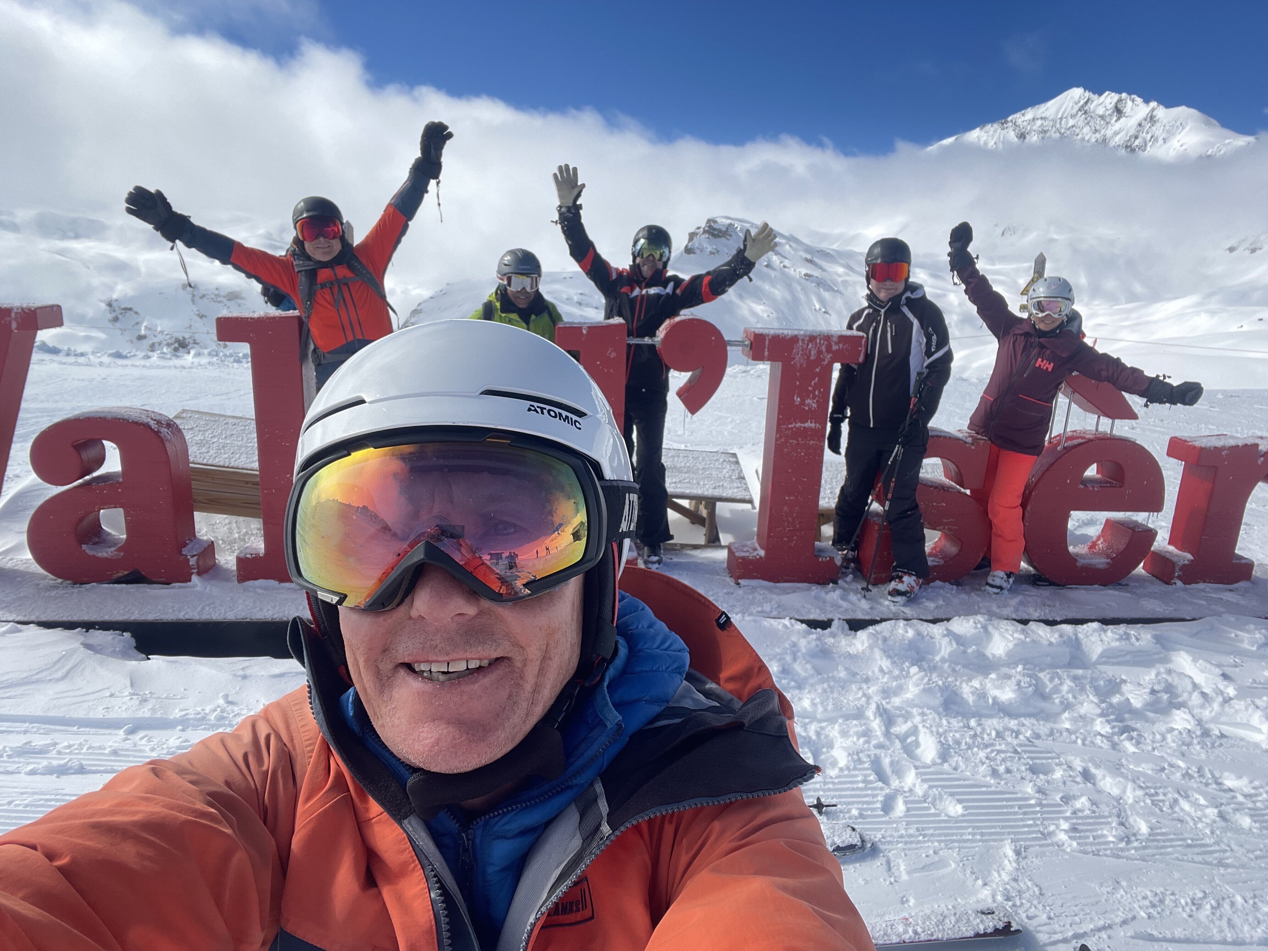 Henry Druce taking selfie in front of Val d'Isere letters with 5 skiers waving in background