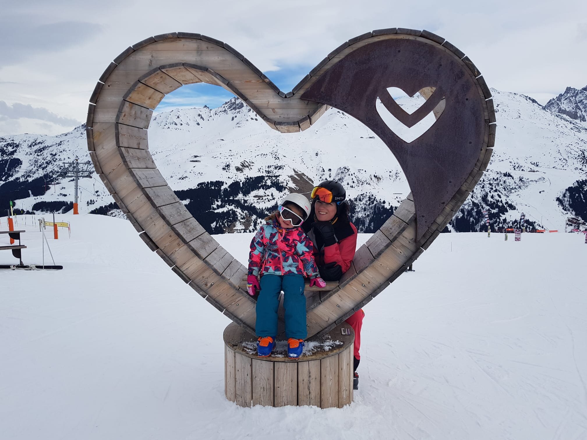 Ski Mindset Coach Kate Casali and daughter posing for ski photo in wooden heart on the ski slopes