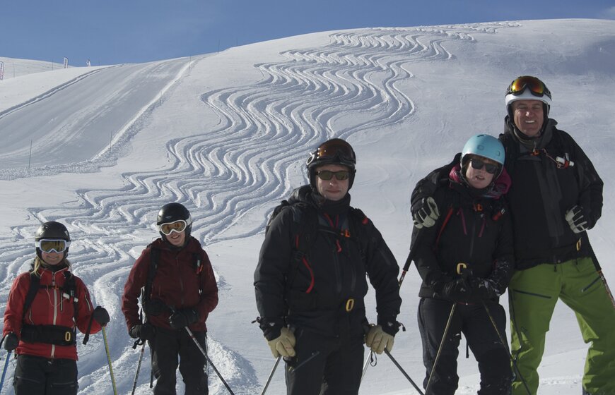 Group of smiling skiers with off-piste ski tracks behind them next to ski piste