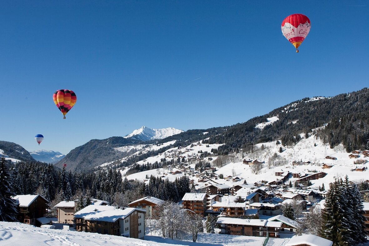 3 hot air balloons flying up above a snowy Les Gets