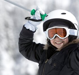 Child in ski helmet and goggles waving ski poles in the air