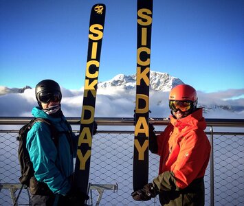 two people holding skis up with mountains in background 