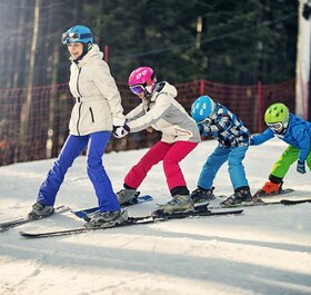 Mum snowploughing down ski slope with 3 children holding on to her