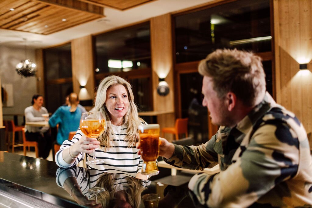 Smiling couple sitting at bar in Bear Lodge raising glass to each other