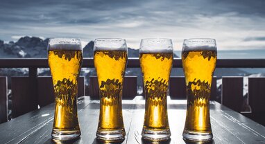 Four glasses of beer with snow capped mountains in the distance