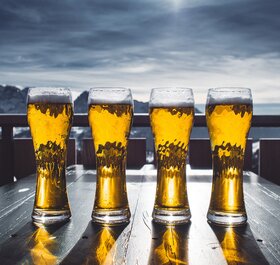 Four glasses of beer with snow capped mountains in the distance